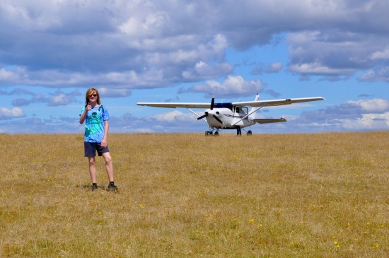 A teenage boy stands in front of a Cessna at the airstrip on Maria Island